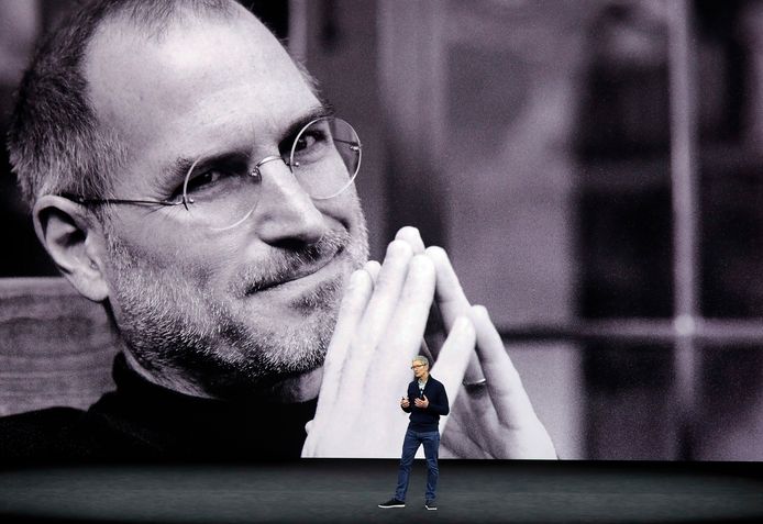 Huidig Apple-CEO Tim Cook met een grote foto van Steve Jobs in de achtergrond.