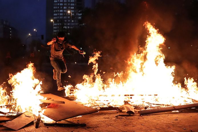 Een demonstrant springt over een brandende barricade in Santiago.