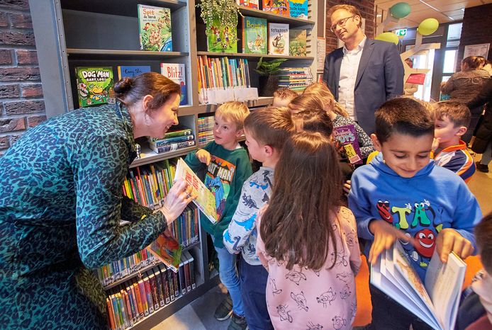 Leesconsulent Cindy van de Loop maakt kinderen van De Tuimelaar in Veghel wegwijs in de net door wethouder Menno Roozendaal (achteraan) geopende schoolbibliotheek.