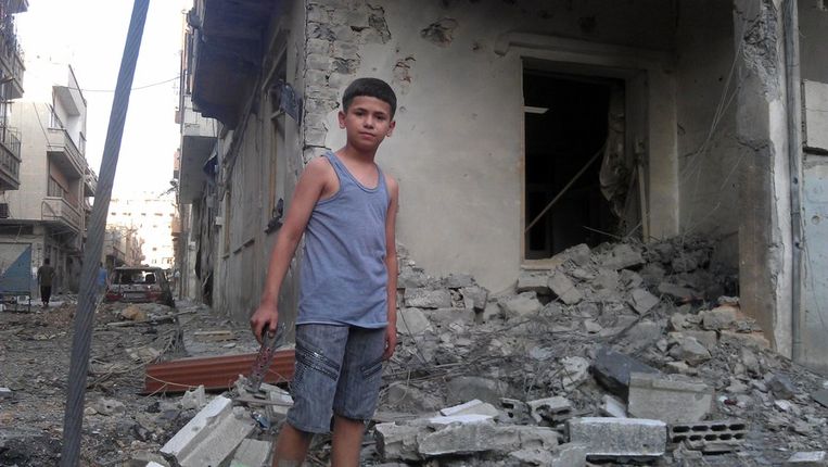 Een jongetje staat voor zijn vernielde huis in de stad Homs, dat in dezelfde provincie ligt als het dorp dat is aangevallen. Beeld afp