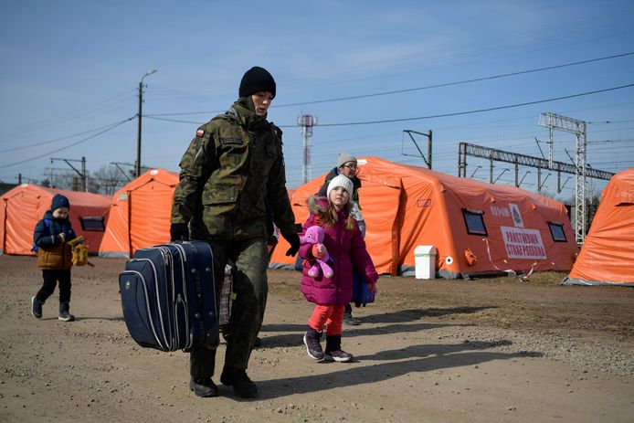 Een Poolse militair helpt een Oekraïense familie met hun bagage in een vluchtelingenkamp aan de grens.