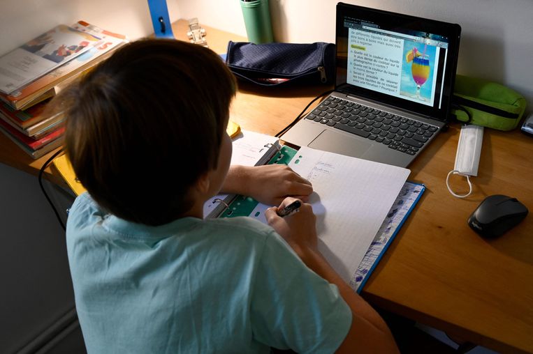 Een leerling maakt zijn huiswerk achter een laptop en op papier. Beeld AFP