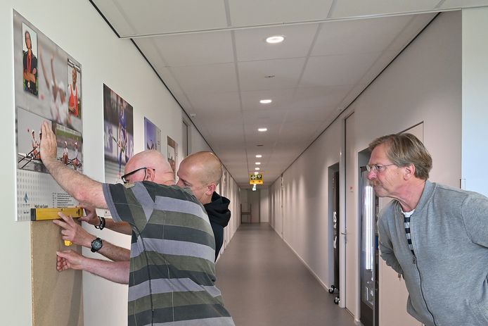 Personeel druk met het ophangen van de foto's voor de Wall of Fame, Jan Kottink kijkt toe.