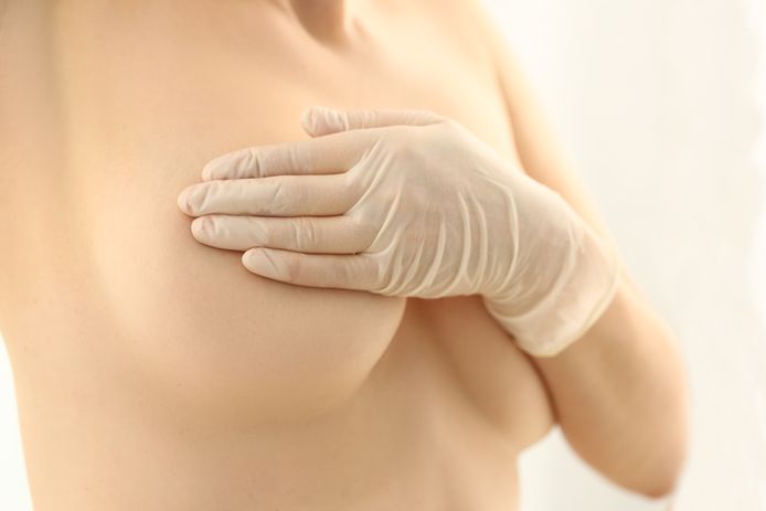 Woman hand in rubber gloves and naked female breast. Enlargement and breast lift concept