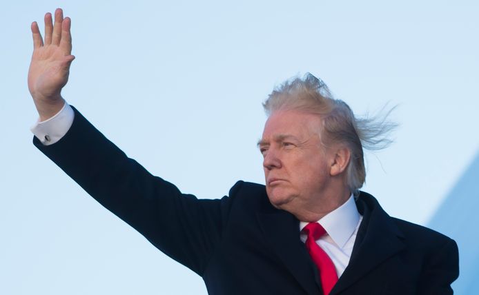 Donald Trump zwaait terwijl de wind met zijn haren speelt.