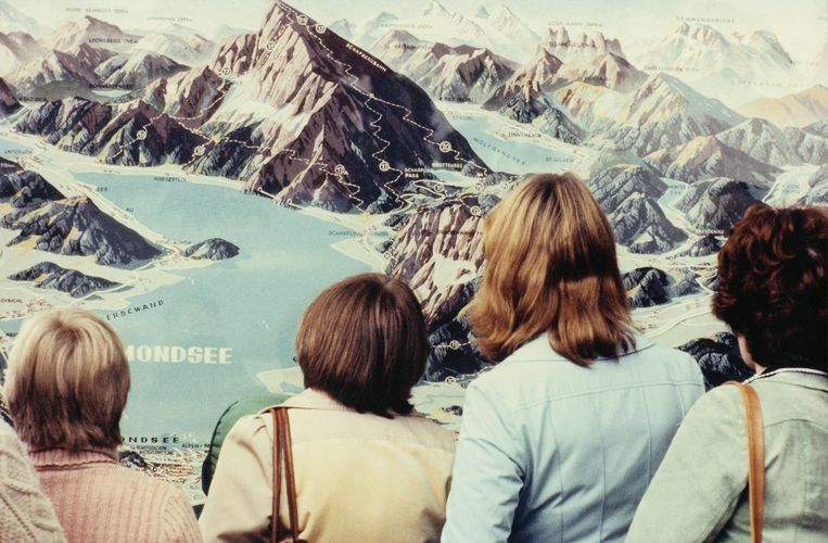 Salzburg, 1977. Vier vrouwen kijken naar een grote, realistische landschapskaart van een bergachtig gebied.  Beeld Luigi Ghirri