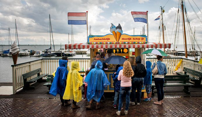 Toeristen met paraplu’s trotseren de regen in de oude haven van Volendam.