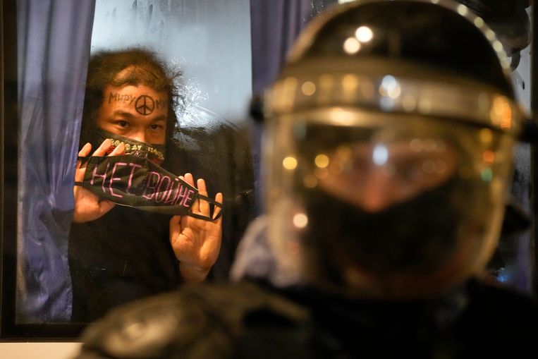 Een aangehouden demonstrant in Moskou toont vanuit de bus haar mondkapje met daarop: 'Geen oorlog'. Beeld AP