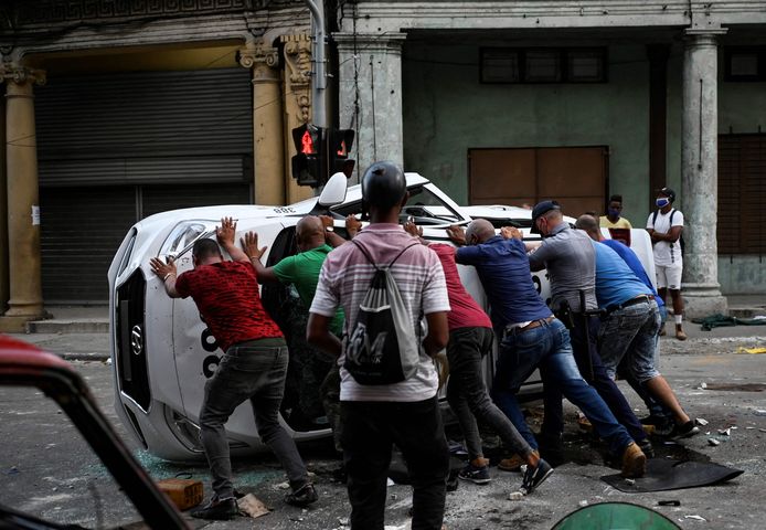 TOPSHOT - People push an overturned car in the street in the framework of a demonstration against Cuban President Miguel Diaz-Canel in Havana, on July 11, 2021. - Thousands of Cubans took part in rare protests Sunday against the communist government, marching through a town chanting "Down with the dictatorship" and "We want liberty." (Photo by YAMIL LAGE / AFP)