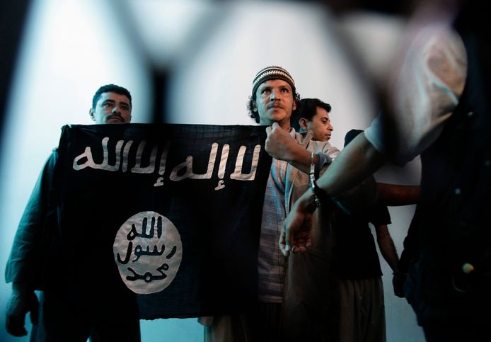 Sur cette photo d'archives du mardi 23 avril 2013, un militant yéménite présumé d'Al-Qaïda, au centre, tient une bannière islamiste alors qu'il se tient derrière les barreaux lors d'une audience devant la cour de sécurité de l'État à Sanaa, au Yémen. L'arabe sur le drapeau indique : "Il n'y a pas d'autre Dieu qu'Allah et Mohammed est le messager de Dieu."