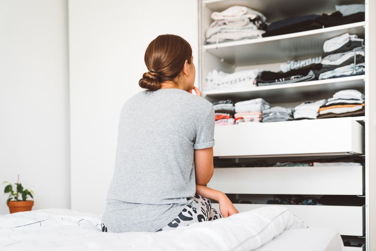 View from the back, woman sitting on the edge of the bed looking at her closed, deciding what to wear. Beeld Getty Images