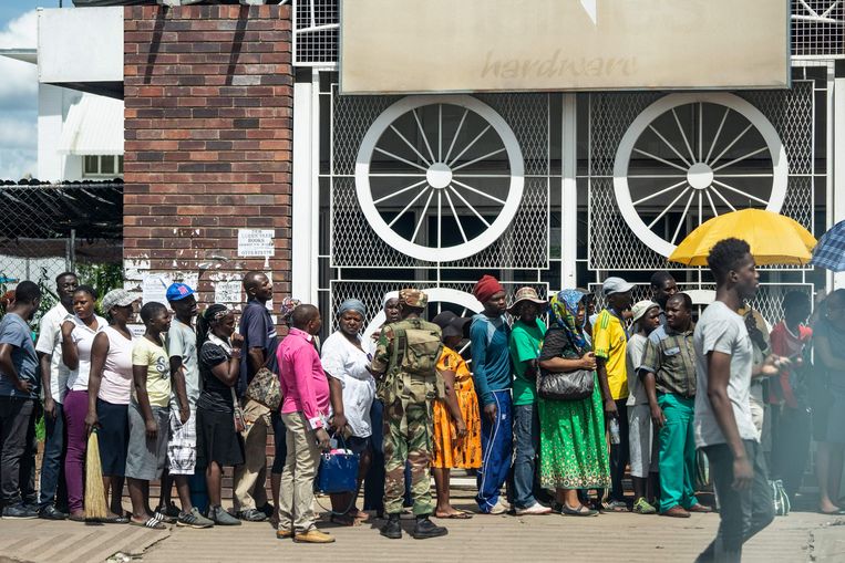 Onder toezicht van veiligheidstroepen staan mensen in de rij voor een supermarkt in de hoofdstad Harare.  Beeld AFP