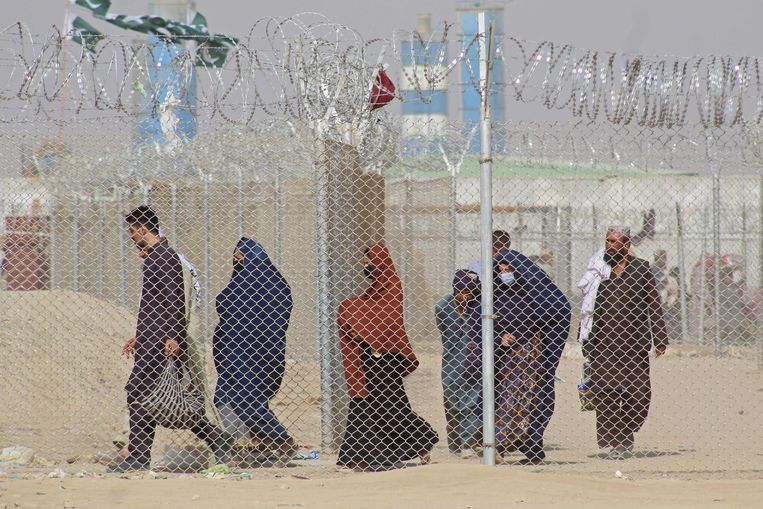 Afghanen lopen voorbij een hek met prikkeldraad. Er dreigt een humanitaire crisis. Beeld AFP