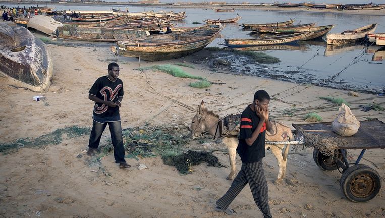Twee jonge mannen lopen door de haven van de Mauritaanse hoofdstad Nouakchott. In de haven worden regelmatig vissersboten gestolen of verkocht aan migranten die de gevaarlijke overtocht over zee willen wagen naar de Canarische eilanden. Beeld Guus Dubbelman / de Volkskrant