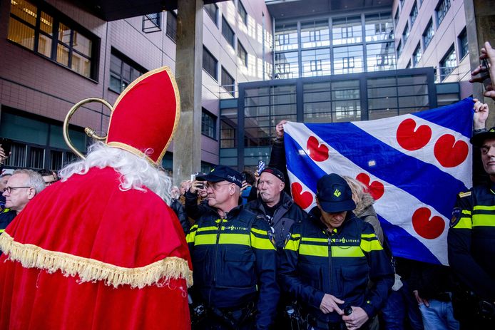 Een sympathisant van de ‘blokkeerfriezen’ mocht verkleed als Sinterklaas de zitting in Leeuwarden niet bijwonen. Andere sympathisanten zwaaien met de Friese vlag.