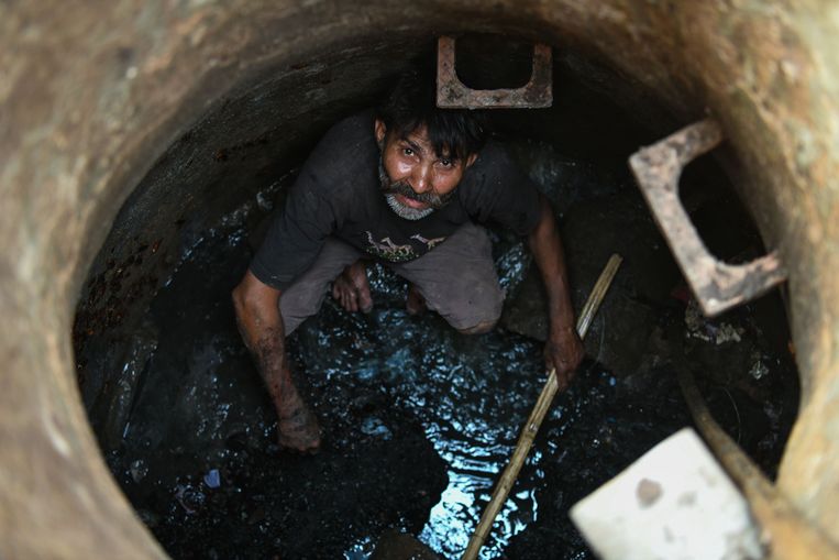 Een dalit aan het werk in een beerput in New Delhi. Beeld AFP