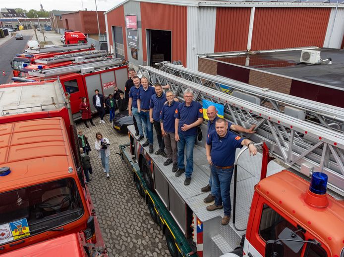 Jan ten Berge (uiterst rechts) en zijn mannen op het konvooi brandweervoertuigen. Anne Kroes is de vierde van links. Op de grond onder meer pers en andere belangstellenden.