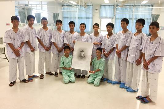De twaalf voetballertjes en hun coach met een schets van de omgekomen duiker, de Thai Samarn Kunan.