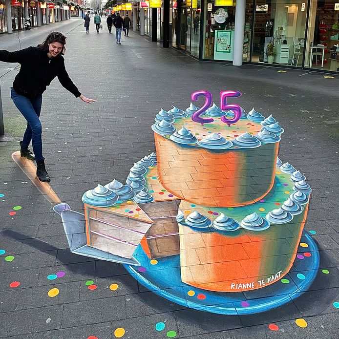 Een bezoeker poseert met de grondschildering van de taart.