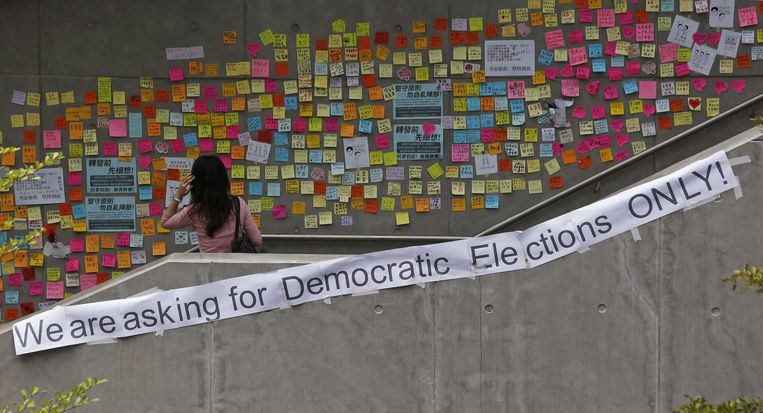 Een vrouw kijkt naar de kleurrijke briefjes die demonstranten hebben opgehangen op een voetgangersbrug in Hongkong. Beeld reuters