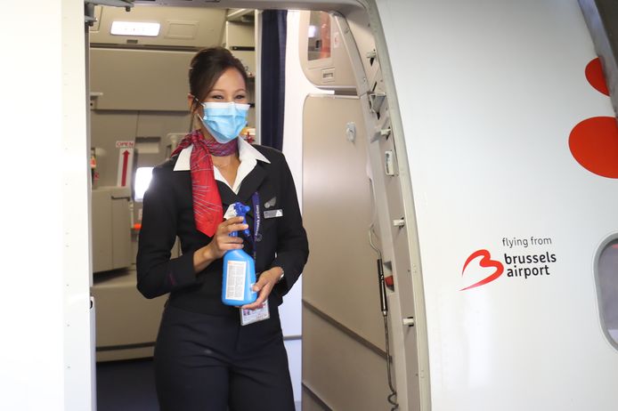 Een stewardess met mondmasker en desinfecterende gel.