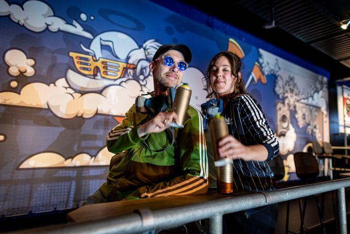 Op het balkon van de Jupiler Stage van Metropool ‘proosten’ Don Slizerone en Nina Paintina met hun spuitbussen op een geslaagde klus. Ze hebben hier aan een luchtthema gewerkt.