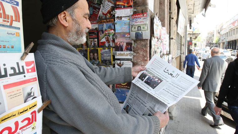 Een man leest vandaag de krant op straat in Damascus. Beeld afp