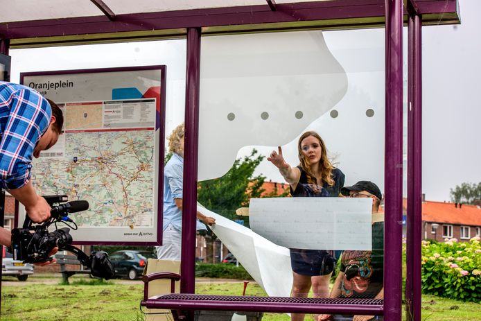 Melissa Vermeule geeft aanwijzingen bij het beplakken van het bushokje aan het Oranjeplein.