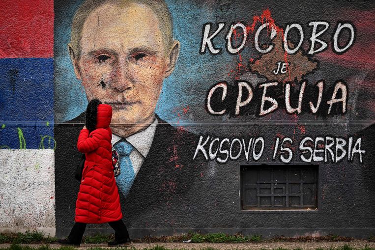 Wandelaar in Belgrado en een muurschildering van de Russische president Vladimir Poetin. Daarbij de tekst 'Kosovo is Servië'. Beeld AFP