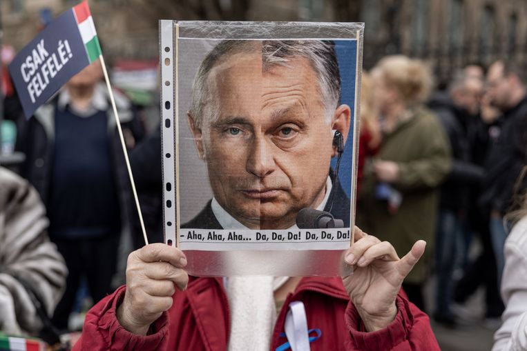Aanhangers van de Hongaarse oppositiekandidaat Peter Marki-Zay houden een protestbord omhoog waarop de gezichten van de Hongaarse premier Orbán en de Russische president Poetin zijn te zien. 
  Beeld Getty Images