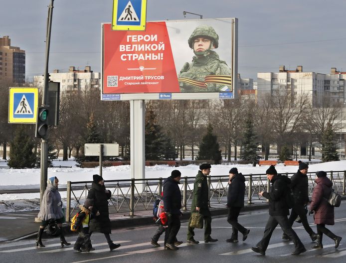 Mensen steken een straat over onder een reclamebord  met de slogan 'Glorie aan de helden van Rusland’ in Sint-Petersburg.