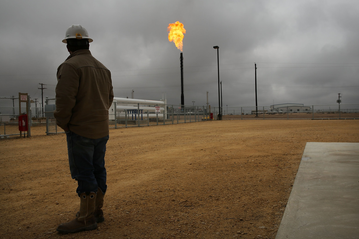 Een werknemer van Apache Corporations kijkt in het Texaanse Garden City naar de gasvlammen van het stoken van het overtollige aardgas. Beeld Getty
