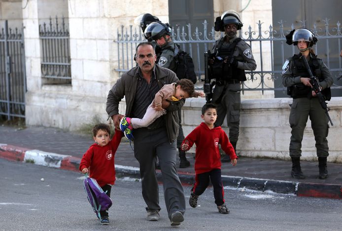 Een Palestijnse man en kinderen wandelen voorbij Israëlische soldaten in Bethlehem.
