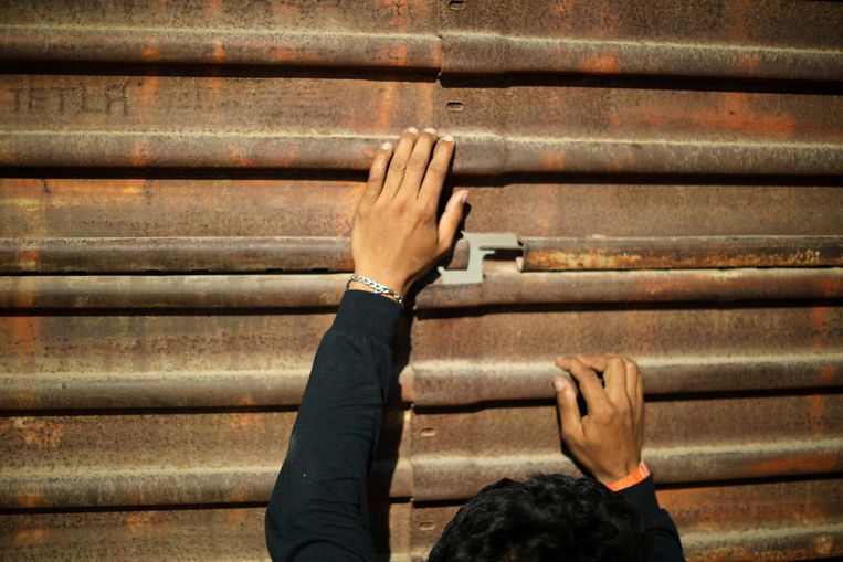 Een migrant, die als onderdeel van de migrantenkaravaan vanuit Midden-Amerika naar de VS is getrokken, probeert Amerikaanse grenswachten te bekijken door een gat in de muur in Tijuana, Mexico, 25 november 2018. Beeld Reuters