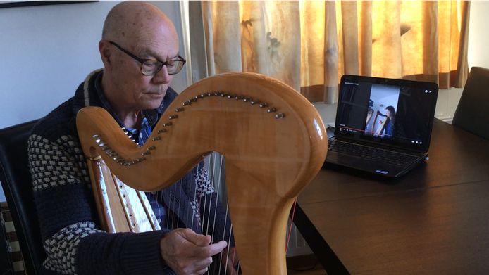 Deelnemer Bart (73) volgt thuis harples. In het beeldscherm zien we harpdocente Beate Loonstra.