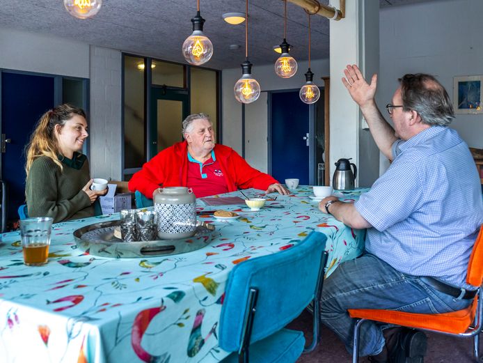 Bewoners Veerle van Dieren, Gerrit Pars en Pim Walenkamp (van links naar rechts) aan de eettafel in een gemeenschappelijke ruimte van de experimentele flat aan de Sao Paulodreef in Overvecht. Op de achtergrond de deur naar de hal van de  trappengang.