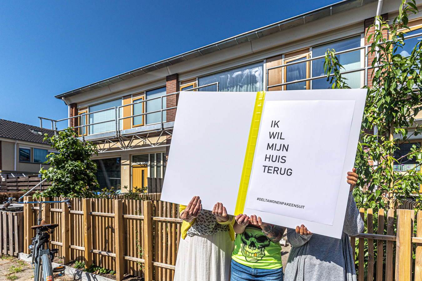 Bewoners in Holtenbroek voor hun huizen met de tekst 'Ik wil mijn huis terug’ in een zwartboek, dat is aangeboden aan deltaWonen.