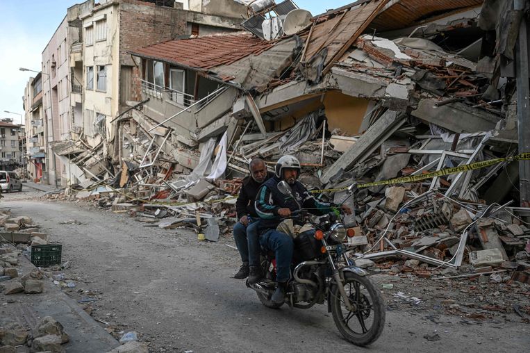 Mensen rijden op een motor door de verwoeste straten van Hatay, een van de zwaarst getroffen gebieden in Turkije.  Beeld AFP