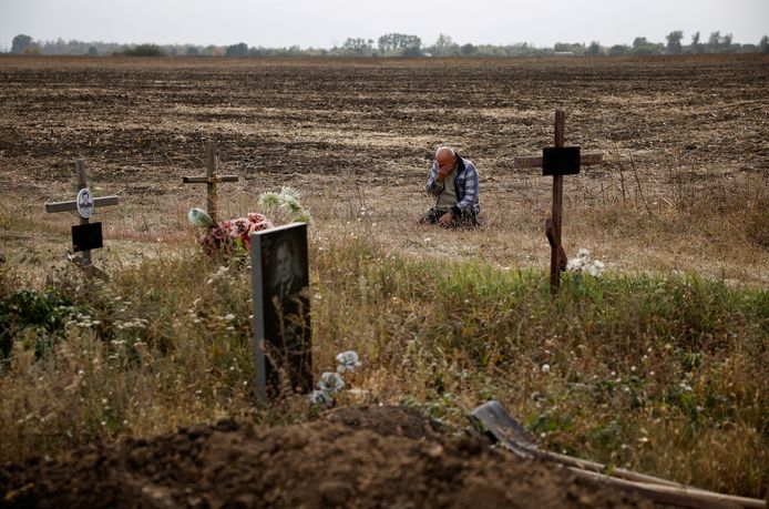 Een 61-jarige man naast graven terwijl hij rouwt na de dood van zijn dochter en andere familieleden die omkwamen bij de aanval in Hroza.