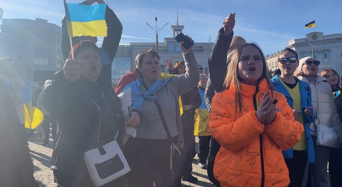 Gewikkeld in blauw-gele vlaggen scanderen tientallen mensen in Cherson leuzen als “Glorie aan Oekraïne” en “Glorie aan de Natie”.