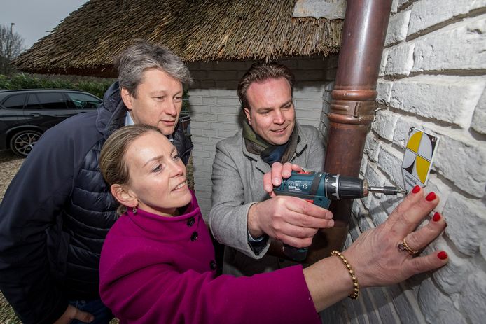 Wethouder Frank Groen schroeft met hulp van Astrid Bongers-Lubberink het monumentenbordje op de muur van de villa in Tiel, onder toeziend oog van haar man.