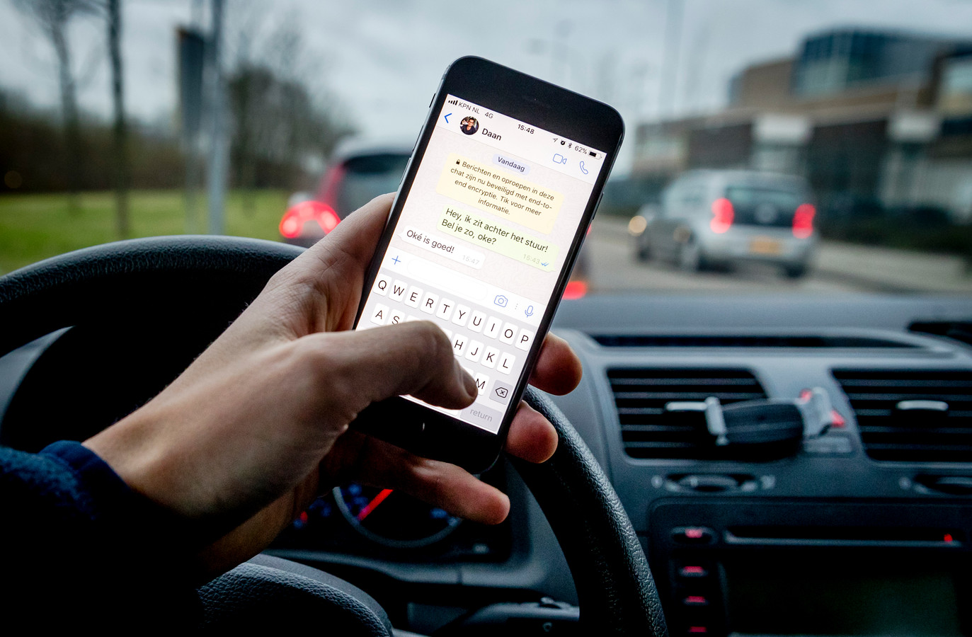 Een bestuurder verstuurt een bericht met zijn mobiele telefoon tijdens het rijden in de auto.