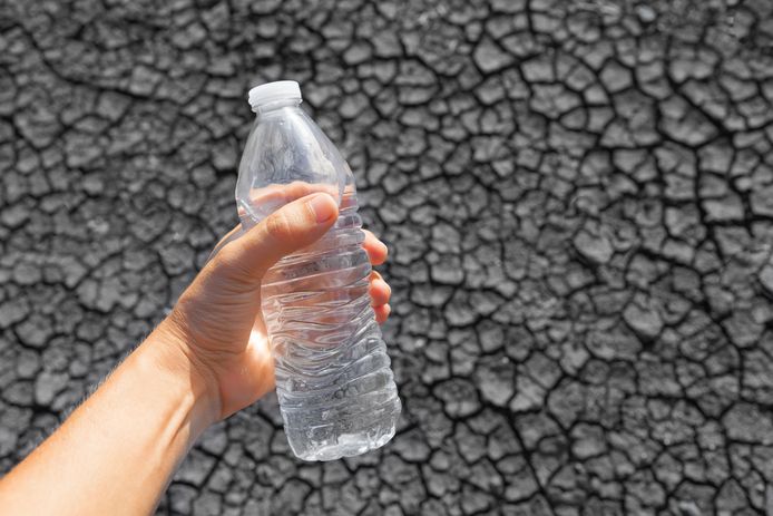 Man holding up bottle of water against a dried desert landscape.