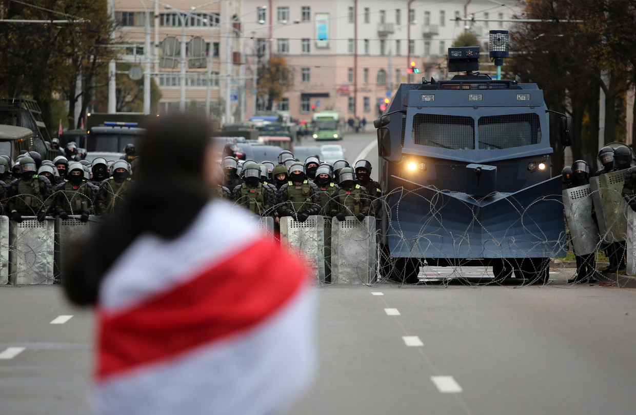 Een demonstrant met een vlag staat tegenover politiemannen die de weg blokkeren tijdens een protest tegen president Loekasjenko in Minsk. Beeld EPA