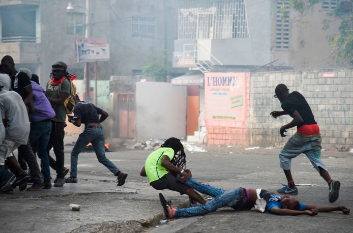 Een man valt terwijl hij het lichaam van een dode kameraad mee wil slepen tijdens protesten in de Haitiaanse hoofdstad.