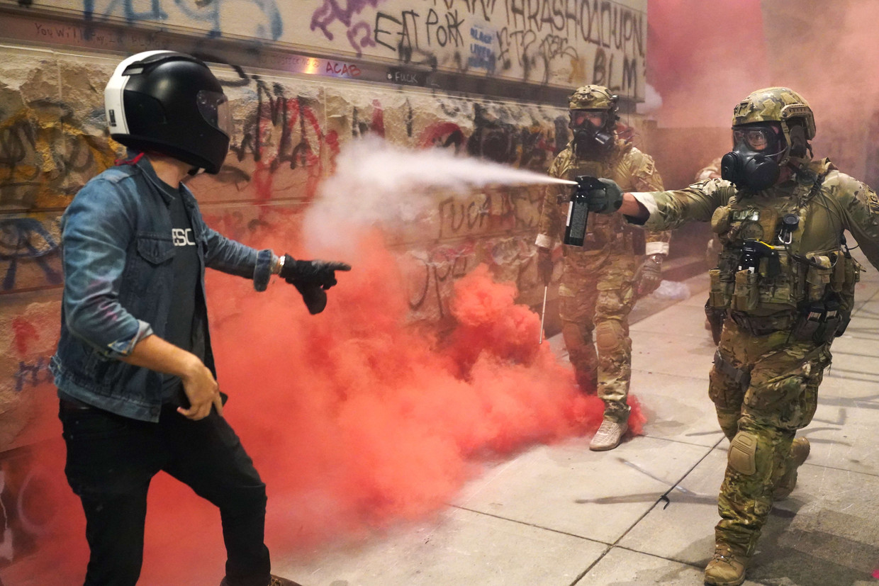 Een officier in camouflagekledij spuit pepperspray naar een demonstrant in Portland, Oregon. Beeld AFP