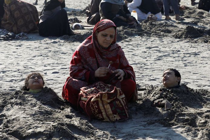 Een vrouw zit naast twee kinderen die tot het hoofd zijn ingegraven in het zand. In Pakistan heerst het bijgeloof dat dit tijdens een zonsverduistering voor genezing kan zorgen.