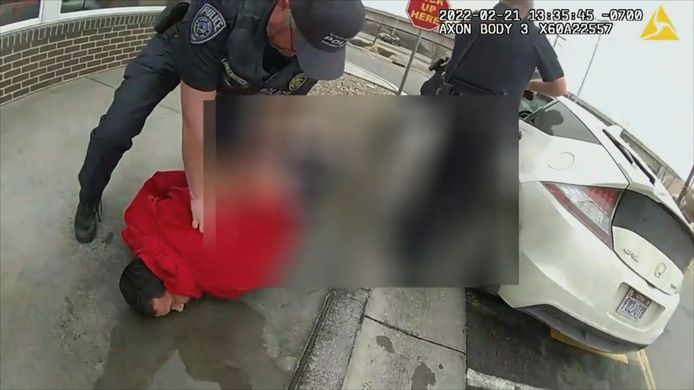 De jongen schiet vanuit de auto terwijl zijn vader door agenten op de grond wordt gedrukt.