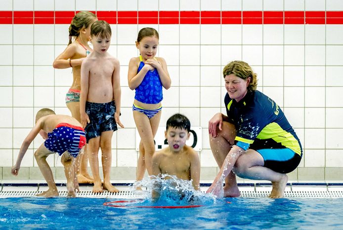 Een docent geeft aanwijzingen tijdens een zwemles voor kinderen in een zwembad voor het behalen van de Nationale Zwemdiploma.