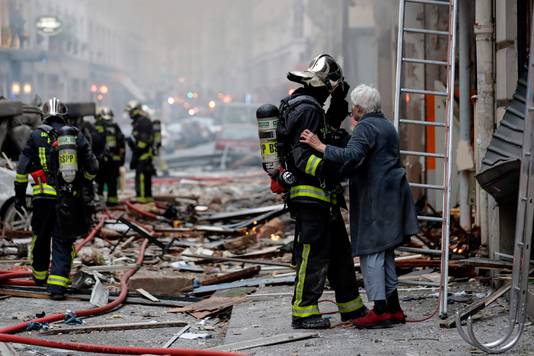 Een oudere dame wordt door een brandweerman in veiligheid gebracht.